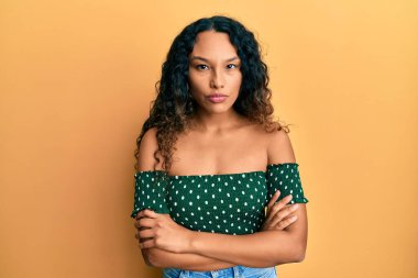 Gündelik kıyafetler giyen, kuşkucu ve gergin genç Latin bir kadın. Yüzünde çapraz kollarla onaylamayan bir ifade var. negatif kişi. 