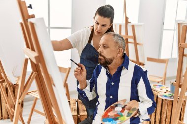 Genç resim öğretmeni kadın sanat stüdyosundaki tuvalde resim yapan yaşlı adama resim öğretiyor.