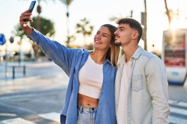 Genç adam ve kadın çift gülümsüyor. Kendilerine güveniyorlar. Sokakta akıllı telefonun yanında selfie çekiyorlar.