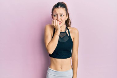 Spor kıyafetleri giyen genç esmer kadın gergin ve gergin görünüyor. Ağzı tırnak yiyen ellerle. anksiyete. 