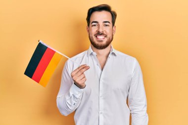 Handsome caucasian man with beard holding germany flag looking positive and happy standing and smiling with a confident smile showing teeth 