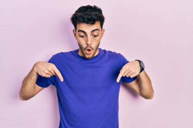 Gündelik tişört giyen genç İspanyol adam parmaklarını göstererek reklamı gösteriyor, şaşırmış yüz ve ağzı açık. 