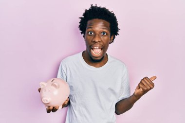 Genç Afrikalı Amerikalı domuz kumbarası tutan ve ağzı açık gülümseyen bir adam. 
