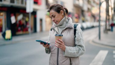 Orta yaşlı İspanyol kadın akıllı telefon kullanıyor. Sokakta kahve içiyor.