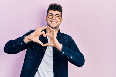 Gündelik kıyafetler ve gözlük takan, aşık gülümseyen, elleriyle kalp sembolü yapan genç İspanyol bir adam. romantik kavram. 