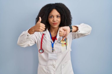 Genç Afro-Amerikan kadın doktor üniforması giyiyor ve steteskop takıp baş parmak işareti yapıyor, anlaşmazlık ve mutabakat ifadesi. çılgın çatışma 