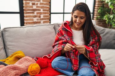 Genç İspanyol kadın gülümsüyor. Kendine güvenen dikiş dikerken evde iğne ve iğne kullanıyor.