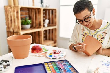 Sanat atölyesinde kilden seramik boyarken gülümseyen genç İspanyol kadın.