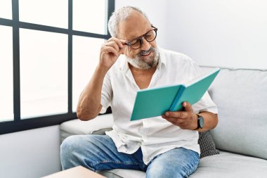 Kıdemli gri saçlı adam evde kendinden emin bir şekilde kitap okuyor.