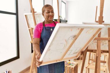 Kıdemli Afro-Amerikan kadın gülümsüyor. Sanat stüdyosunda kendine güvenen bir tablo çiziyor.