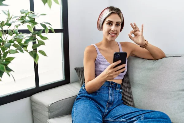 Jovem Mulher Bonita Usando Mensagem Digitação Smartphone Sentado Sofá Sorrindo — Fotografia de Stock