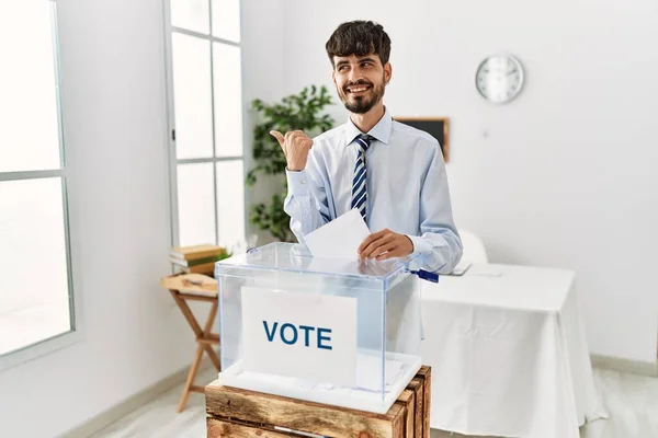 満面の笑みを浮かべて投票箱の中に包ま投票ひげを生やしているヒスパニック系の男顔を見て 親指で側面を指してアップ — ストック写真