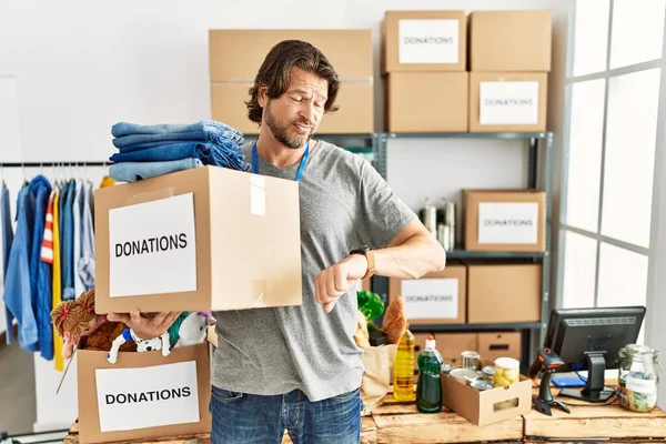 Gönüllü olarak bağış kutusunu tutan yakışıklı orta yaşlı bir adam kol saatini kontrol ediyor, rahat ve kendinden emin. 