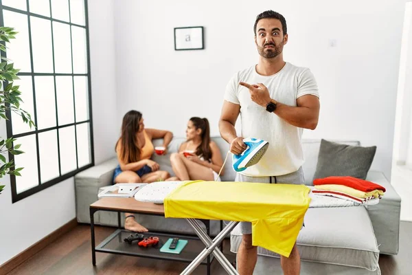 Young Hispanic Man Ironing Clothes Home Pointing Aside Worried Nervous — стоковое фото