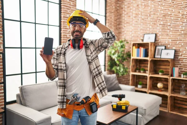Young Hispanic Man Beard Working Home Renovation Holding Smartphone Stressed — стоковое фото