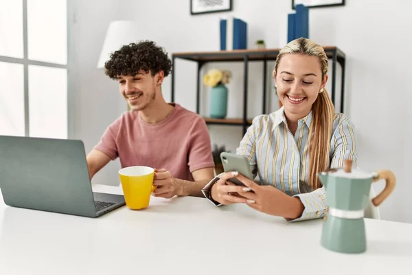 在家里用笔记本电脑和智能手机喝咖啡的年轻夫妇 — 图库照片
