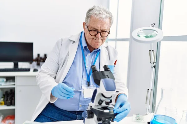 研究室で顕微鏡を使う科学者の制服を着た中世の白髪の男 — ストック写真