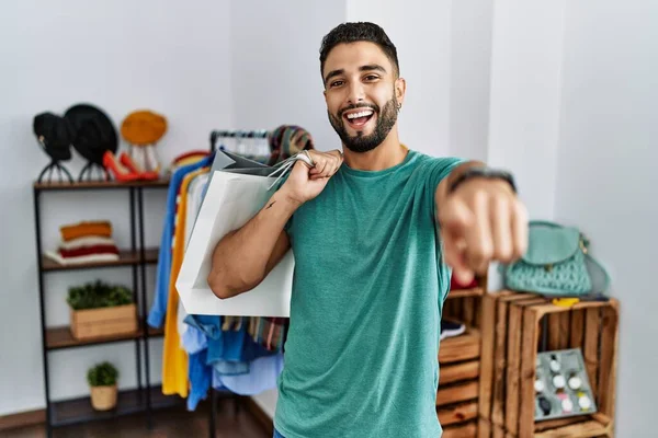 Alışveriş poşetlerinde sakallı genç yakışıklı adam seni ve kamerayı işaret ediyor, gülümsüyor, pozitif ve neşeli. 