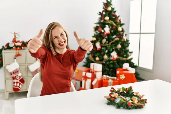 Kavkazská Mladá Blondýnka Sedící Stole Vánočního Stromku Schvalující Pozitivní Gesto — Stock fotografie