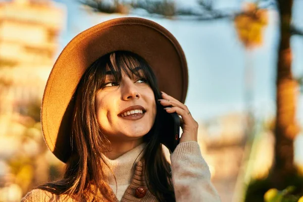 Kışlık şapkalı esmer kadın parkta telefonda gülümsüyor.