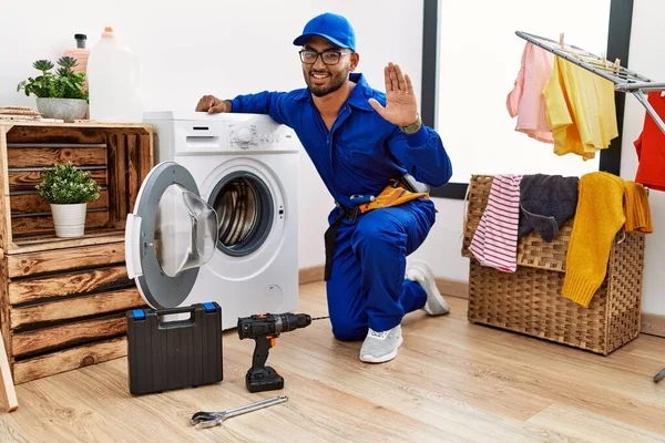 Çamaşır makinesinde çalışan genç Hintli teknisyen mutlu ve güler yüzlü bir şekilde selam veriyor. 