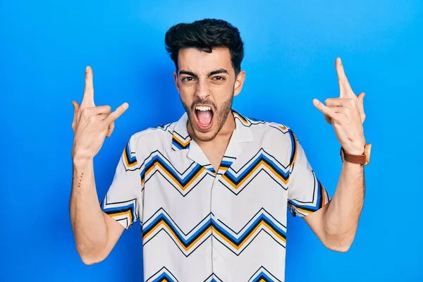 Latin asıllı genç adam, gündelik kıyafetler giyip çılgın bir ifadeyle bağırıyor ve elleri havada rock sembolü yapıyor. Müzik yıldızı. ağır müzik konsepti. 