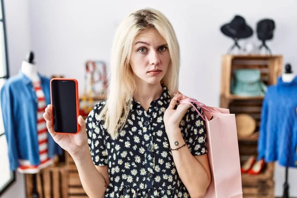 Young Blonde Woman Holding Shopping Bags Showing Smartphone Screen Skeptic — Foto de Stock