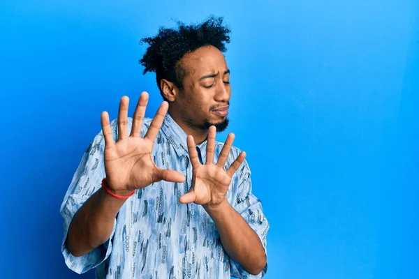 Sakallı genç Afro-Amerikan bir adam. Günlük giysiler giymiş, tiksindirici bir ifade takınıyor ve tiksindirici bir yüz ifadesi takınıyor. Eller havada. 