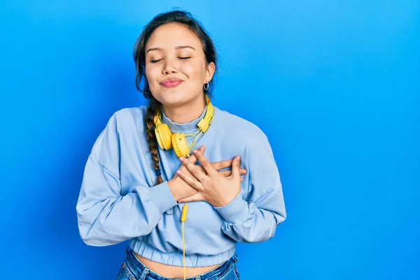 若いヒスパニック系の女の子の音楽を胸に手で笑みを浮かべてヘッドフォンを使用して聞いて 目の顔に感謝のジェスチャーで閉じます 健康の概念 — ストック写真