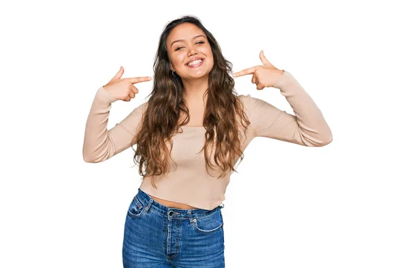 若いヒスパニック系の女の子は陽気な笑みを浮かべてカジュアルな服を着て 指の歯と口を指しています 歯の健康の概念 — ストック写真