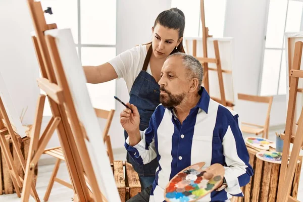 Genç resim öğretmeni kadın sanat stüdyosundaki tuvalde resim yapan yaşlı adama resim öğretiyor.