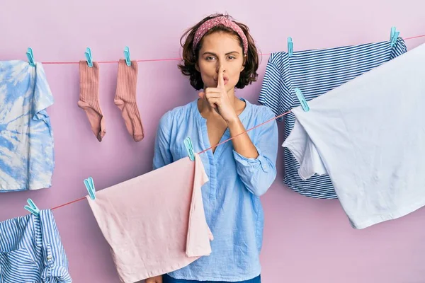 Genç esmer kadın ipin etrafında çamaşır yıkıyor ve dudakları parmaklarıyla sessiz olmak istiyor. sessizlik ve gizli konsept. 