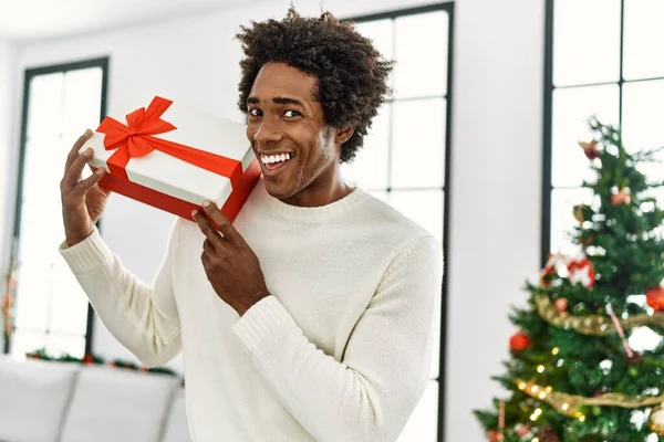 Jong Afrikaans Amerikaans Man Houden Geschenk Stand Door Kerstboom Thuis — Stockfoto