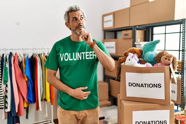 Bağışta gönüllü tişört giyen orta yaşlı İspanyol bir adam bir soru hakkında endişeli ve gergin bir şekilde duruyor. 