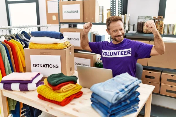 Orta yaşlı bir adam dizüstü bilgisayarla çalışırken gururla gülümseyen kol kaslarını gösteriyor. fitness konsepti. 