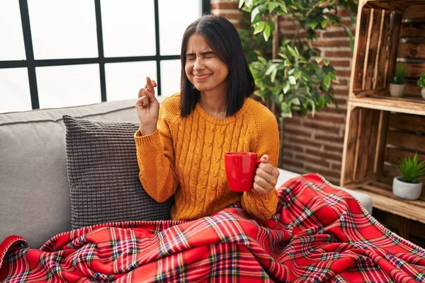 Genç İspanyol kadın kanepede oturup kahvesini yudumlarken parmaklarını çapraz yapıp umut ve gözler kapalı gülümsüyor. Şans ve batıl inançlar. 