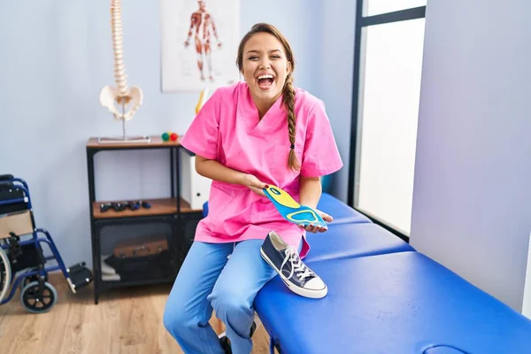 Fizyoterapi kliniğinde elinde ayakkabı tabanı tutan genç İspanyol kadın çılgınlığı kutluyor ve başarı için hayrete düşüyor.. 