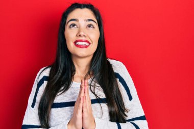 Gündelik giysiler giyen genç İspanyol kız elleri ile yalvarıyor ve dua ediyor. Yüzünde umut ifadesi var. Çok duygusal ve endişeli. Yalvarıyor. 