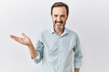 Arka planda sakallı, orta yaşlı İspanyol bir adam. Gülümsüyor, elinde avucuyla kameraya bakıyor.. 