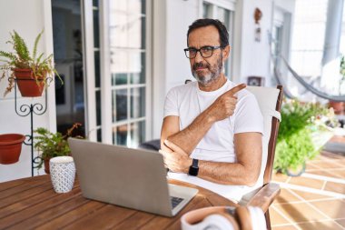 Orta yaşlı bir adam evde bilgisayar kullanıyor. Elleriyle işaret ediyor, ciddi ve sakin bir yüz ifadesi gösteriyor. 