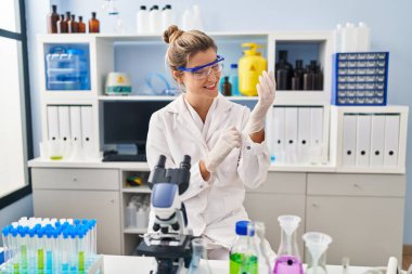 Laboratuvarda bilim adamı üniforması ve eldiven giyen genç sarışın kadın.
