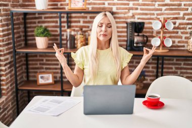 Laptop kullanan genç sarışın kadın evde yoga egzersizi yapıyor.