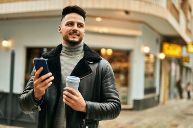 Genç Arap adam akıllı telefon kullanıyor ve şehirde kahve içiyor..