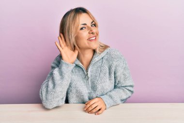 Gündelik giysiler giymiş genç beyaz bir kadın masaya oturmuş sırıtarak kulak misafiri olmuş dedikoduları ya da dedikoduları dinliyor. Sağırlık kavramı. 