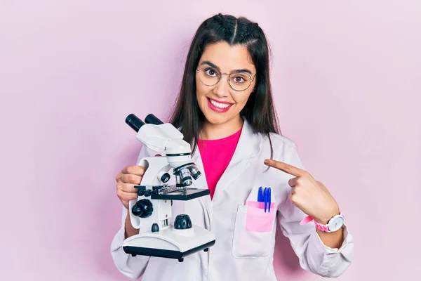 Jovem Hispânica Vestindo Uniforme Cientista Segurando Microscópio Sorrindo Feliz Apontando — Fotografia de Stock