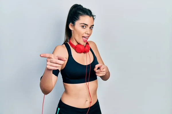 Young Hispanic Girl Wearing Gym Clothes Using Headphones Pointing Fingers — ストック写真