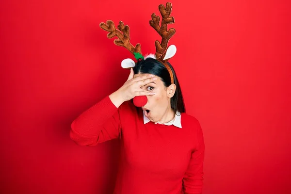 Young Hispanic Woman Wearing Deer Christmas Hat Red Nose Peeking — стоковое фото