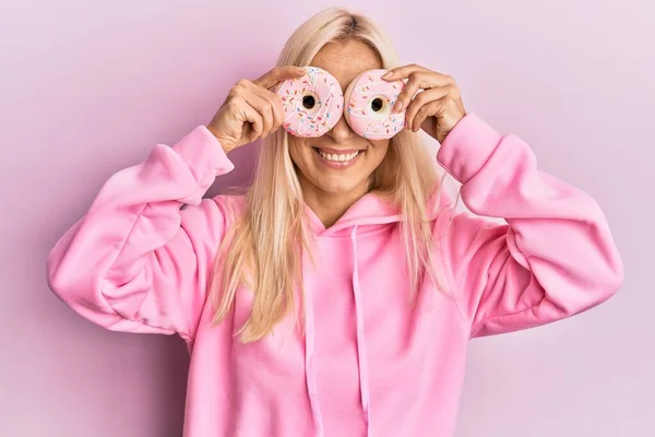 Ung Blond Kvinna Som Håller Välsmakande Rosa Munkar Över Ögonen — Stockfoto