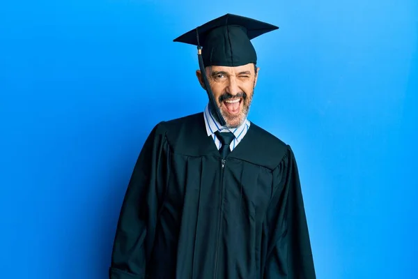 Middle age hispanic man wearing graduation cap and ceremony robe winking looking at the camera with sexy expression, cheerful and happy face. — Stock Image Middle Age Hispanic Man Wearing Graduation Cap Ceremony Robe Winking Royalty Free Stock Photos