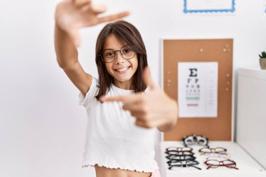 Gözlüklü genç İspanyol kız gülümsüyor ve mutlu yüzlü eller ve parmaklarla çerçeve yapıyor. yaratıcılık ve fotoğrafçılık kavramı. 